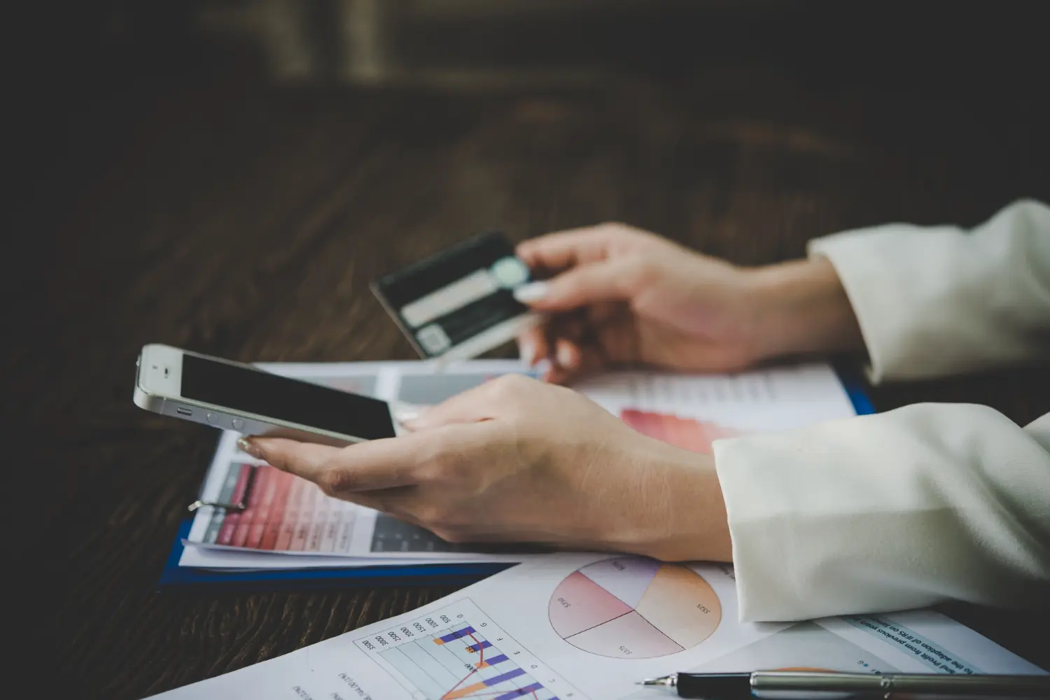ai-payment-reminders-vs-manual-follow-up-singapore Person using a smartphone for payment reminders while reviewing overdue invoices
